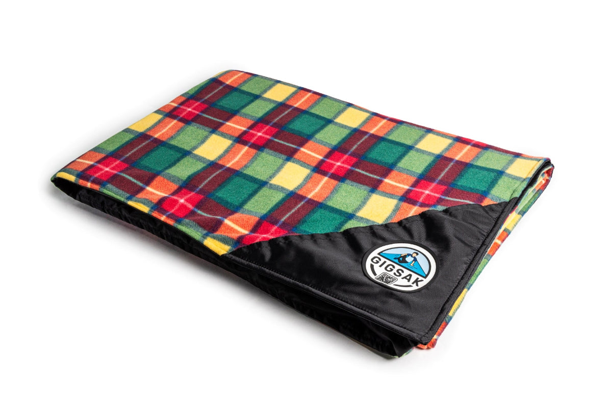 A GIGSAK Giant outdoor waterproof blanket is the only outdoor waterproof blanket you can sit inside. It features a sleek red, orange, yellow, and green tartan with a black waterproof design. GIGSAK features a unique, hidden, cosy shelter to protect against the wind and rain. Simply turn GIGSAK inside out to stay warm and dry. GIGSAK is perfect for family picnics, BBQs, the beach, festivals, open-air cinema, fireworks, camping, and more.