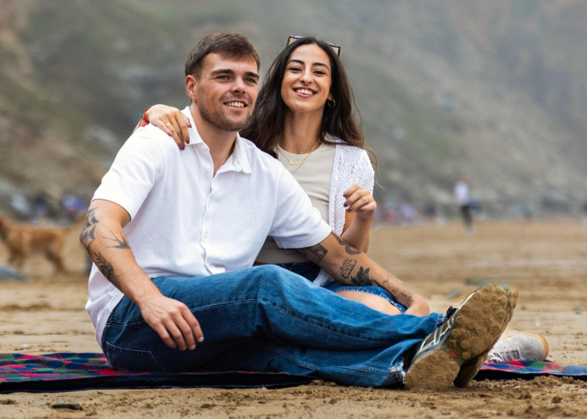 A young couple sat on the beach on a GIGSAK. The GIGSAK outdoor waterproof blanket is the only outdoor waterproof blanket you can sit inside. Features a sleek red, blue, and green coloured tartan with navy blue waterproof design. GIGSAK features a unique, hidden, cosy shelter to protect against the wind and rain. Simply turn GIGSAK inside out to stay warm and dry. GIGSAK is perfect for family picnics, BBQs, the beach, festivals, open-air cinema, fireworks, camping, and more.